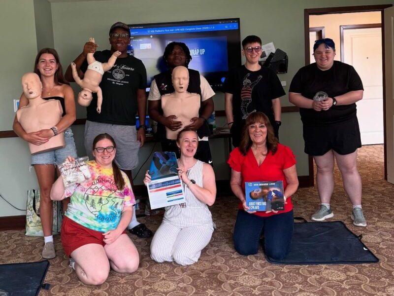CPR-training A group of people in a classroom holding CPR dummies, participating in a first aid training session with certificates and materials.