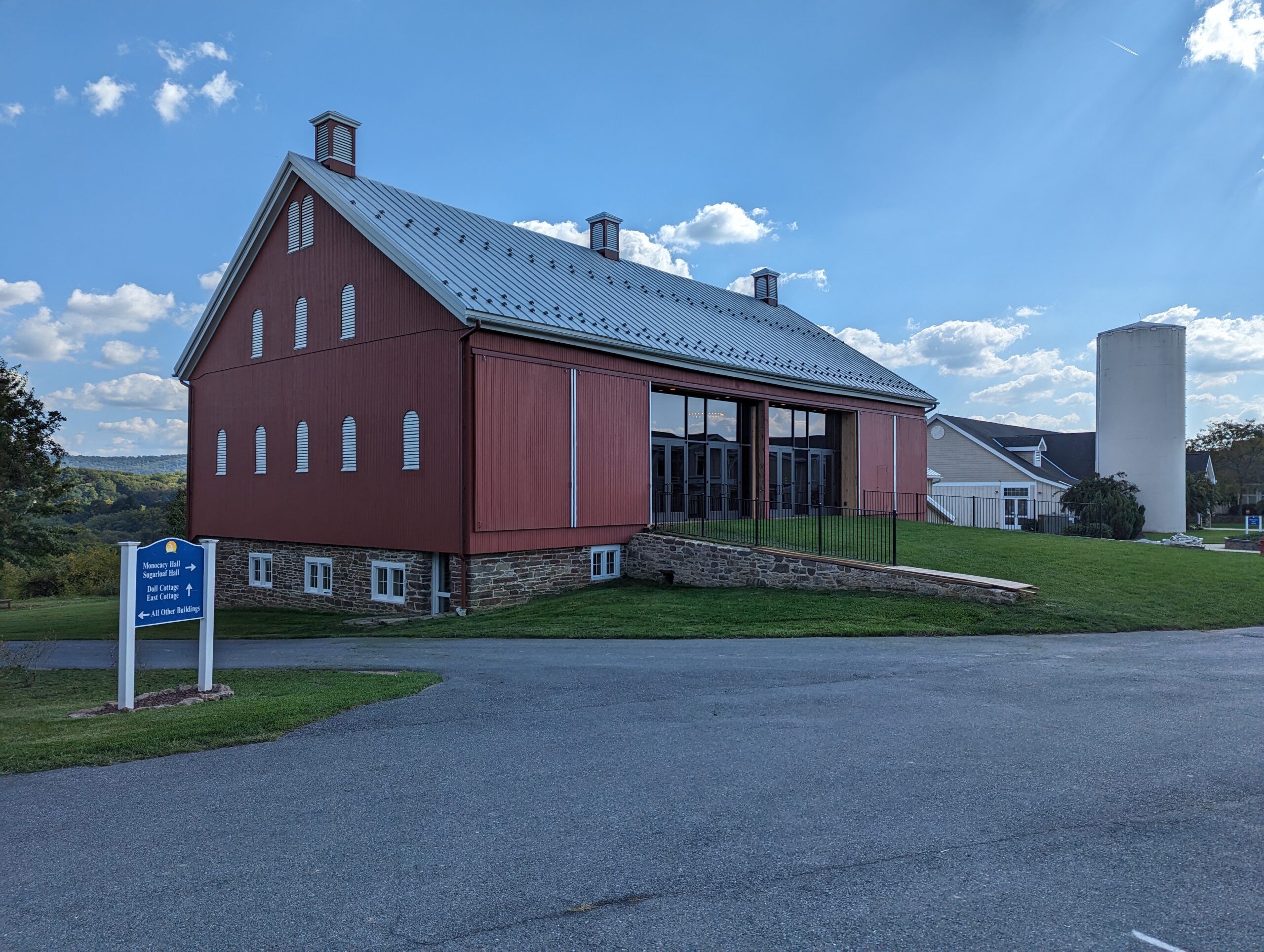 Copy of PXL_20231003_190535664 A red barn-like building with a metal roof, adjacent to a modern facility. Signpost indicates directions to nearby campus locations.