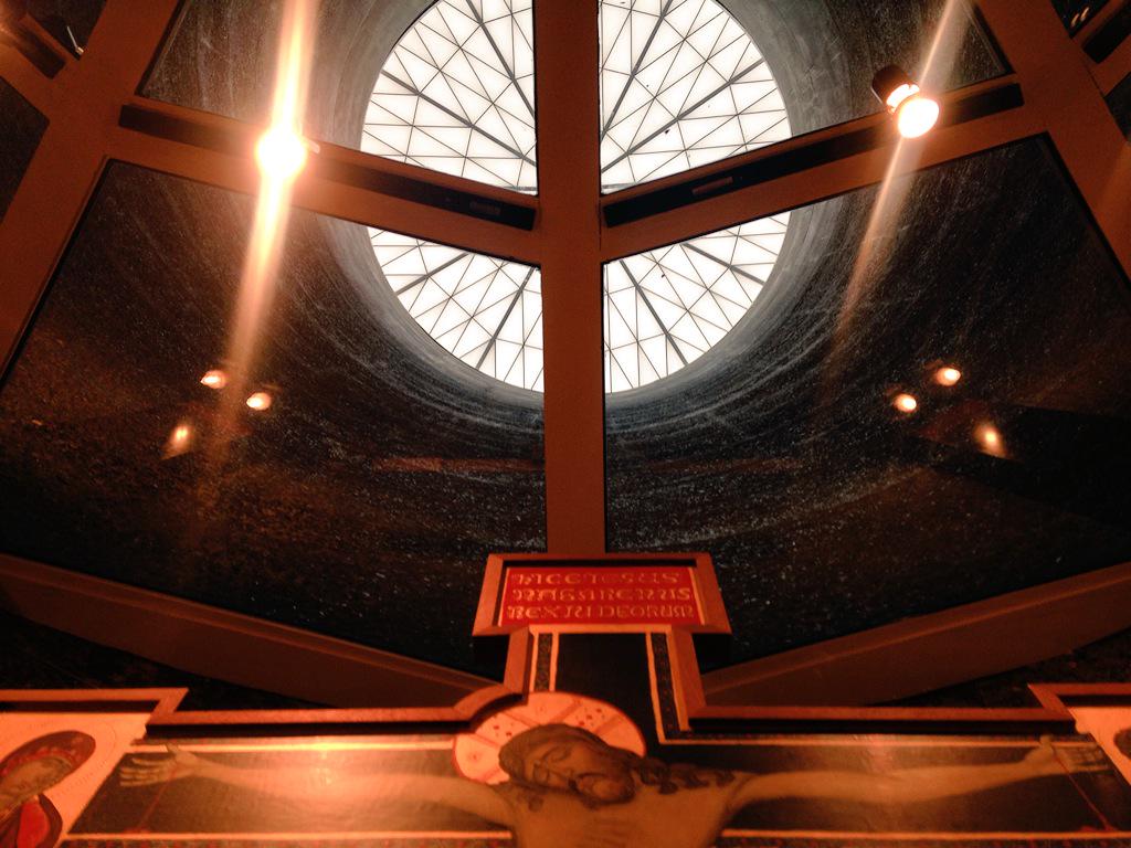 Copy of silo looking up A circular skylight with geometric design illuminates the space below, highlighting a religious artwork featuring detailed, vibrant imagery and inscriptions.