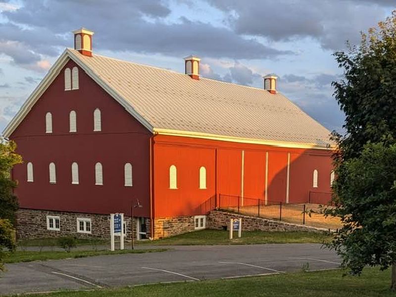 barn photo A large, red barn with white roof vents sits under a partly cloudy sky, surrounded by greenery and parking area.