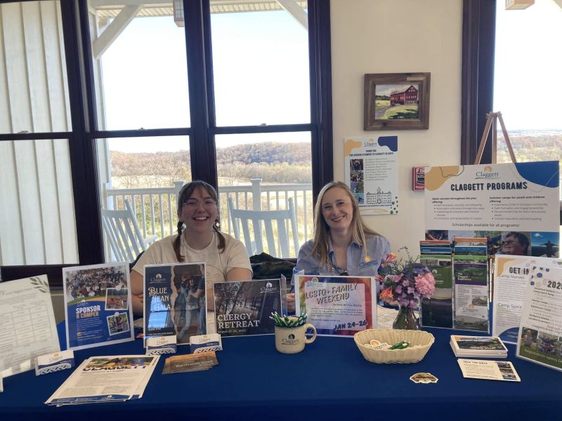 claggett programming Two people sit at a table showcasing pamphlets and posters for Claggett programs, with a scenic landscape visible through the windows behind them.