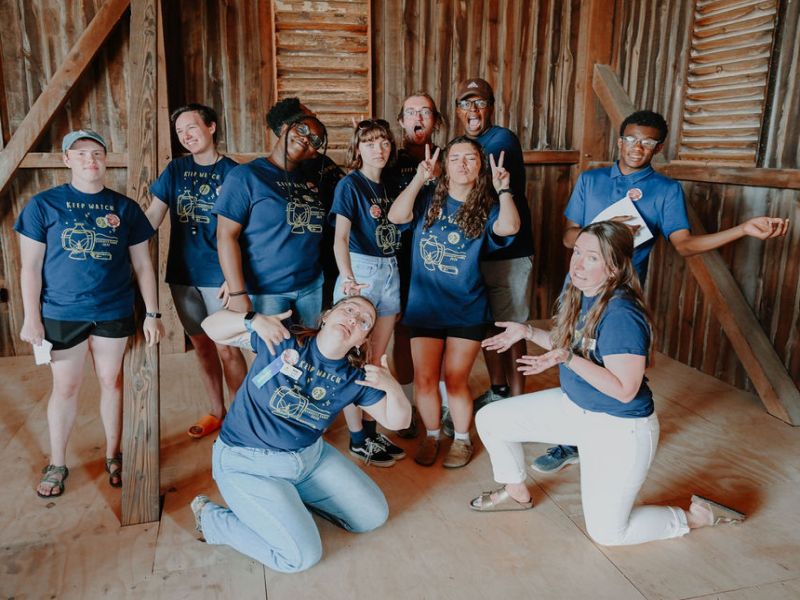 funny group photo A group of ten people in matching blue shirts pose playfully inside a wooden interior, showing varied expressions and gestures.