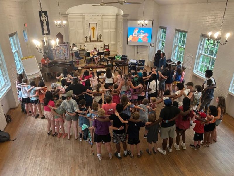 group gathering youth A group of children and people form a circle in a church hall, with musical instruments and a projected screen in view.