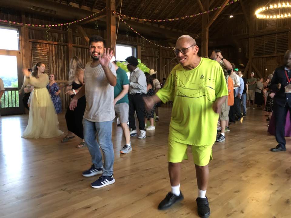 special challenge camp 3 A lively group dances indoors in a rustic setting with wooden beams and string lights, creating a joyful and energetic atmosphere.