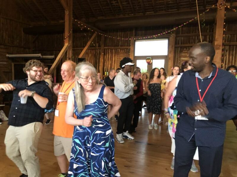 A lively gathering of people dancing in a wooden barn, adorned with string lights, creating a festive and cheerful atmosphere.