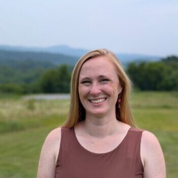 Hannah Graham A person smiling outdoors in a green, mountainous landscape with trees and distant hills under a clear sky. No identifiable landmarks visible.